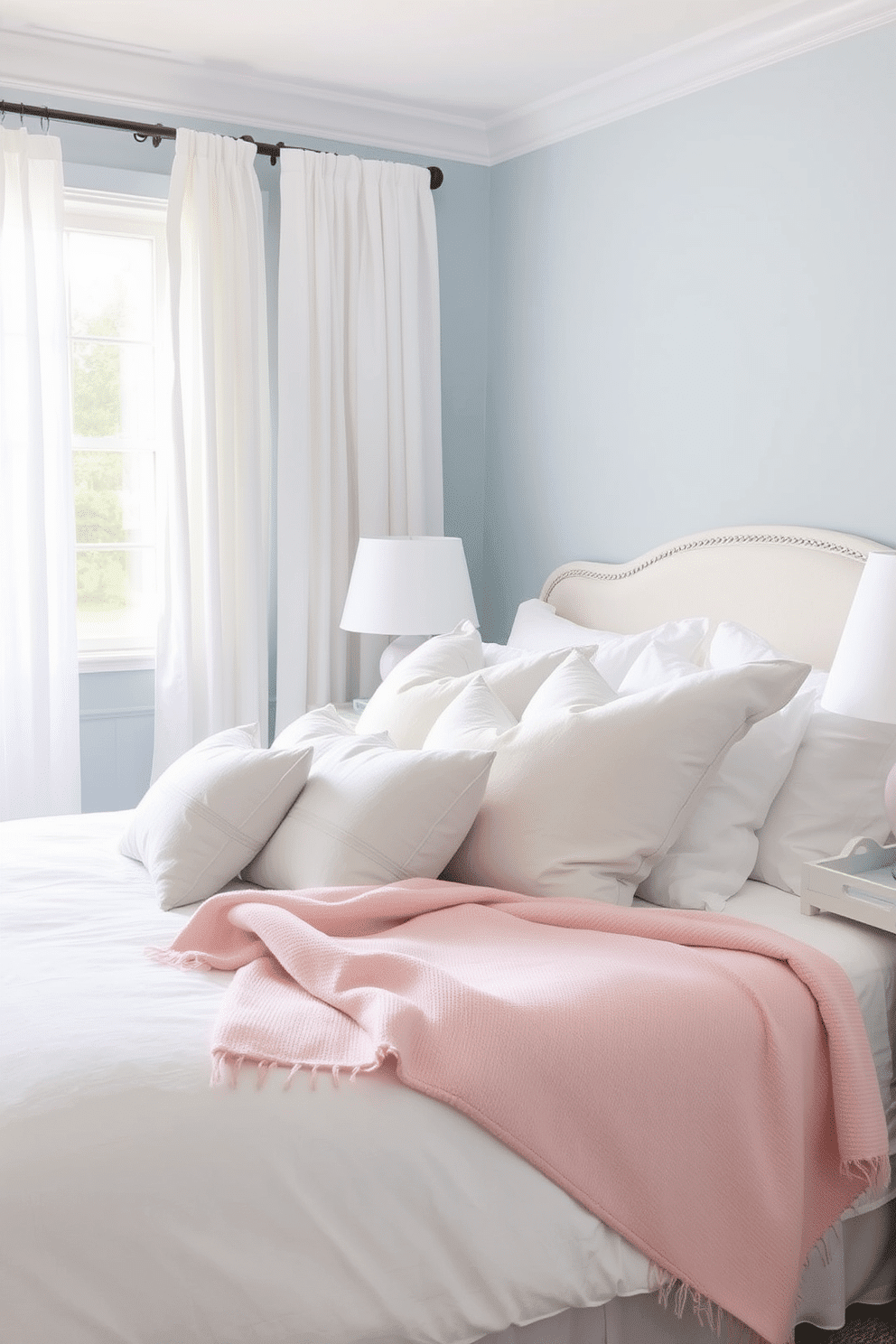 A serene bedroom adorned with dusty blue walls acts as a calming backdrop for an elegant and tranquil space. Soft natural light filters in through sheer white curtains, creating a gentle contrast against the muted tones. Pastel-toned throw pillows and a cozy blush pink blanket are layered atop a crisp white bedspread for added texture and charm. Delicate accents like a pale lavender ceramic lamp and a mint green decorative tray on the nightstand complete the soothing ambiance.
