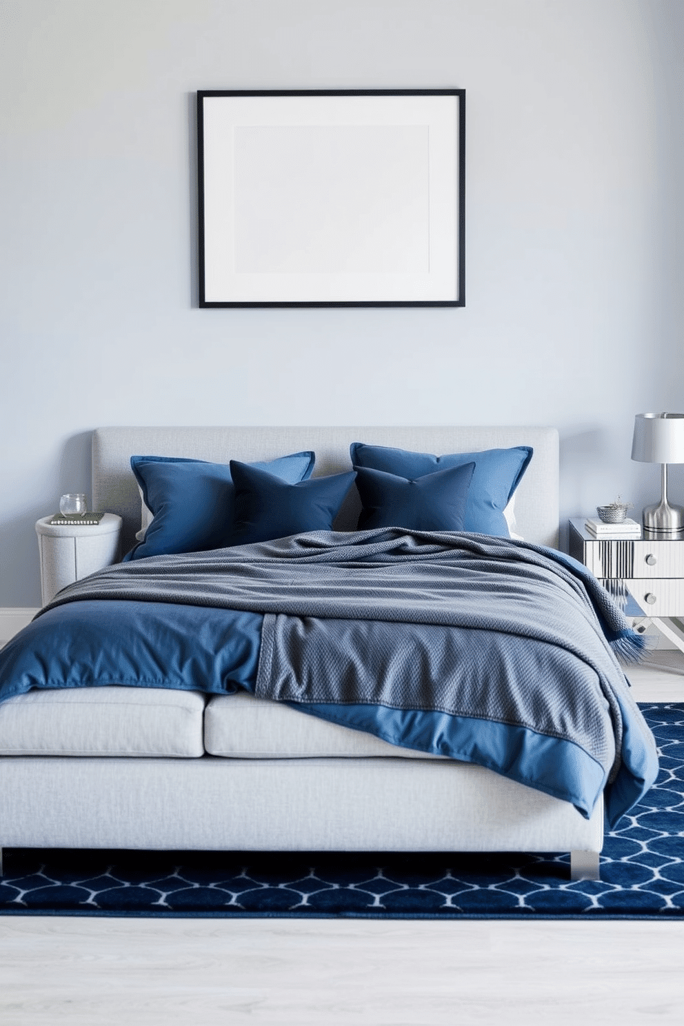 A serene bedroom design with steel blue cushions adorning a soft gray couch that sits effortlessly against a light blue wall. A patterned navy rug grounds the space, complemented by silver-toned accents and a sleek nightstand topped with a modern lamp. The bed features plush steel blue linens with layered gray throws, creating a cozy contrast. Above the bed, a textured headboard and minimalist framed artwork tie together the room's calming and elegant aesthetic.