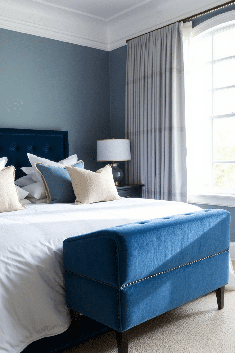 A serene bedroom with soft blue tones as the focal point. A plush blue velvet bench is elegantly positioned by a large window, allowing natural light to cascade across its textured surface. The room features a harmonious blend of muted blue walls paired with crisp white bedding layered with tonal throw pillows. Beside the bench, sheer curtains catch the light breeze, creating an airy and tranquil ambiance perfect for relaxation.