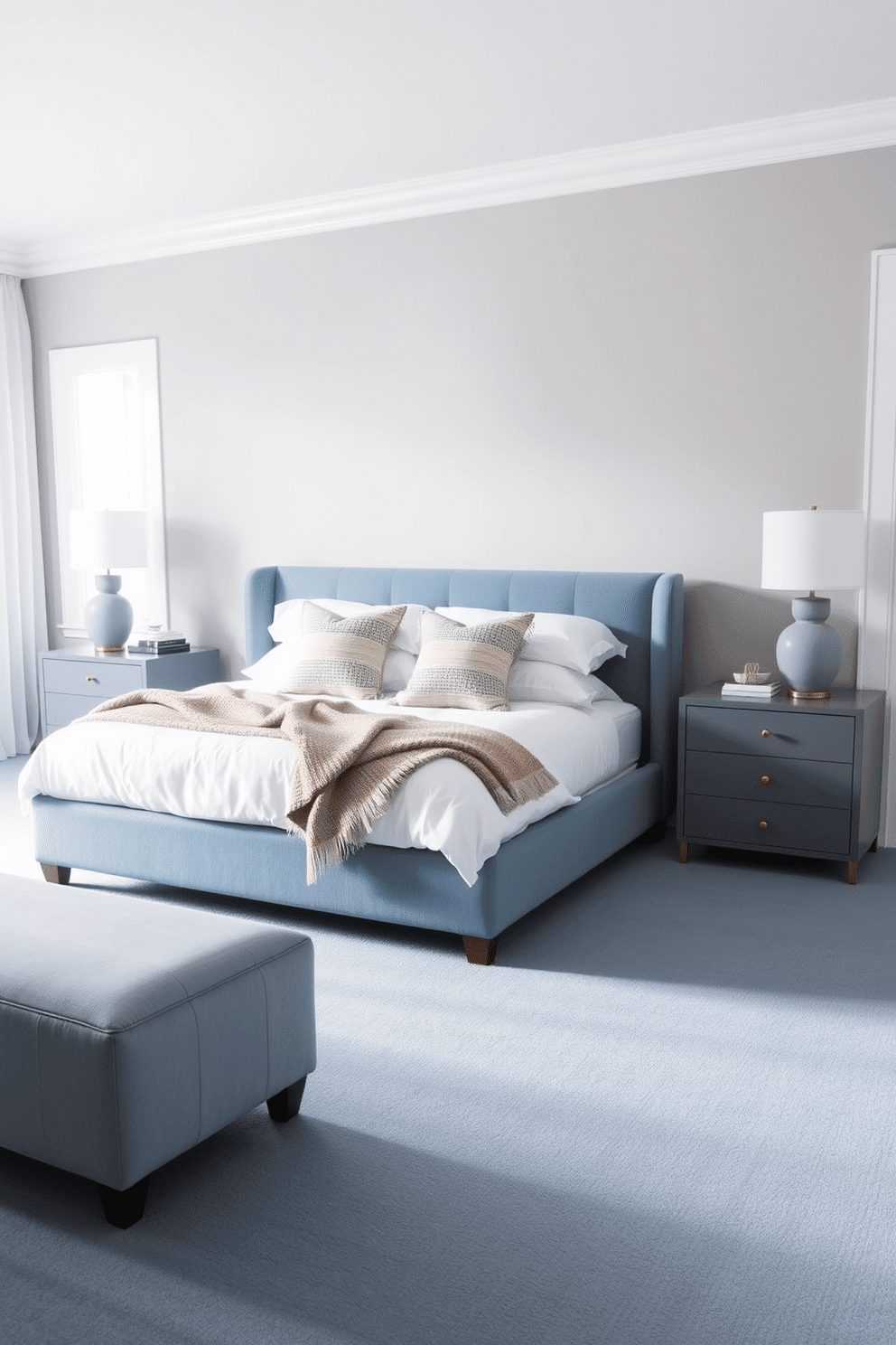 A serene blue bedroom with muted dusty blue carpeting that adds warmth and softness to the space. A low-profile upholstered bed in a matching blue tone rests centrally, with crisp white bedding and layered textured throws. The walls are painted in a soft neutral greige, complementing the blue hues without overwhelming the palette. A pair of sleek gray bedside tables with brass accents hosts understated ceramic lamps, while sheer white curtains diffuse natural light beautifully.