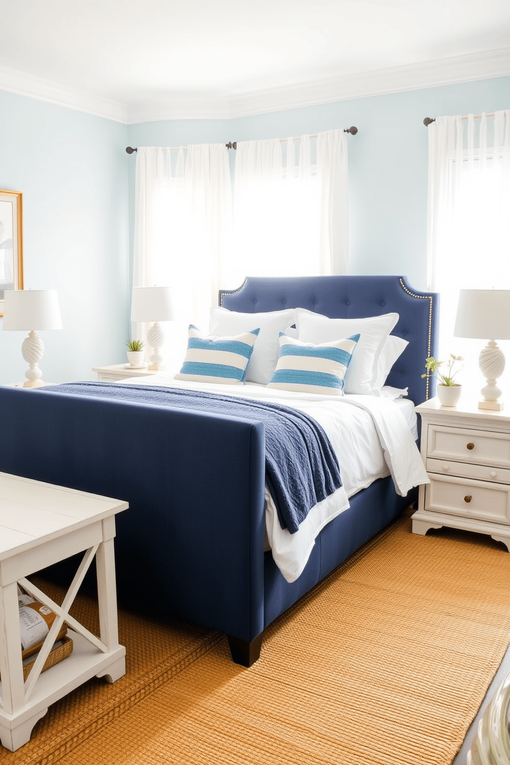 A serene coastal-inspired bedroom adorned with shades of soft sky blue and deep ocean navy. The walls are painted in a light seafoam blue, while a plush upholstered headboard in navy anchors the bed, layered with crisp white linens and striped blue throw pillows. A woven jute rug lies underfoot, adding texture and warmth, while sheer white curtains let in an abundance of natural light. Whitewashed wooden nightstands flank the bed, each topped with a seashell-inspired lamp and small potted greenery for a fresh, natural accent.