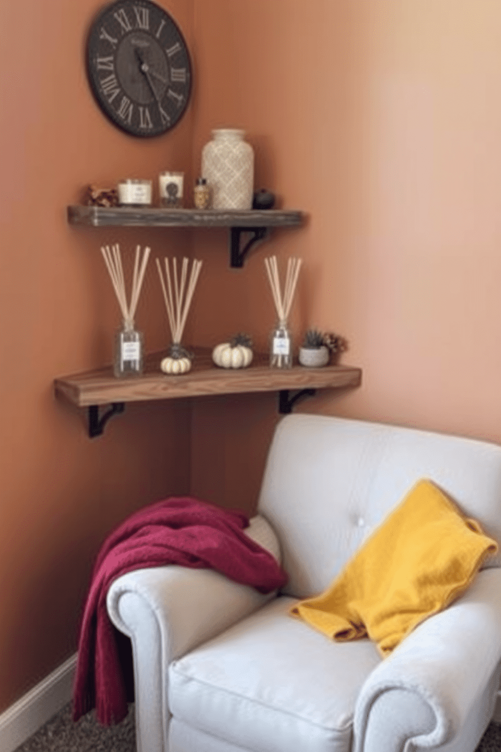 A cozy corner in a small living room featuring seasonal fragrance diffusers that evoke the essence of fall. The diffusers are elegantly arranged on a rustic wooden shelf alongside a collection of autumn-themed decorative items like small pumpkins and colorful leaves. The walls are painted in warm earth tones to enhance the inviting atmosphere. Soft throw blankets in rich burgundy and mustard yellow are draped over a plush armchair, creating a perfect spot to enjoy the comforting scents of the season.