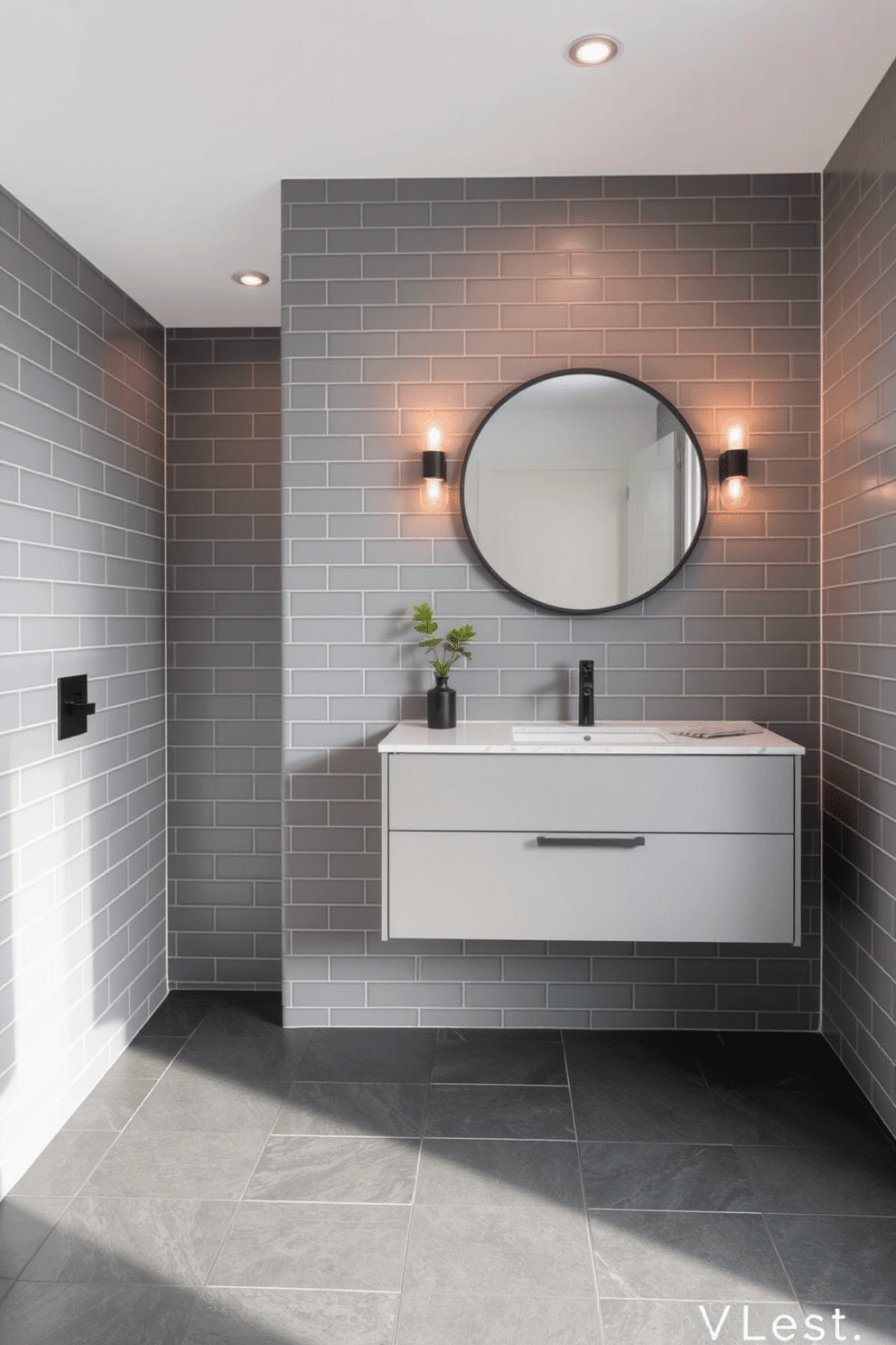 A modern bathroom with gray subway tiles in a matte finish lining the walls, creating a sleek and understated aesthetic. The flooring features large-format charcoal-gray tiles, grounding the space with a cohesive monochromatic look. A floating gray vanity with a quartz countertop adds functionality and style, paired with a circular black-framed mirror above it. Warm ambient lighting and a small potted green plant provide a balance of softness and contrast to the refined gray palette.