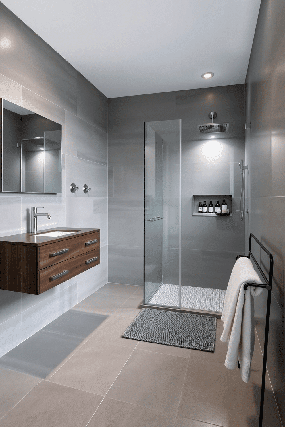 A modern gray bathroom adorned with large-format gray tiles that exude a sleek, seamless surface. The walls and floors are unified with the expansive tiles, creating a clean and minimalist aesthetic. A floating dark wood vanity adds a touch of warmth and contrast, its brushed metal drawer pulls gleaming softly. Above it, a wide frameless mirror reflects the soft glow of recessed lighting for a luxurious ambiance. The shower features a frameless glass enclosure, where the gray tiles continue uninterrupted for a spa-like feel. A built-in niche holds neatly arranged bottles, while chrome fixtures provide a polished finish. Near the vanity, a soft gray woven bath mat complements the muted palette. A simple black metal towel rack, adorned with crisp white towels, completes the effortlessly sophisticated decor.