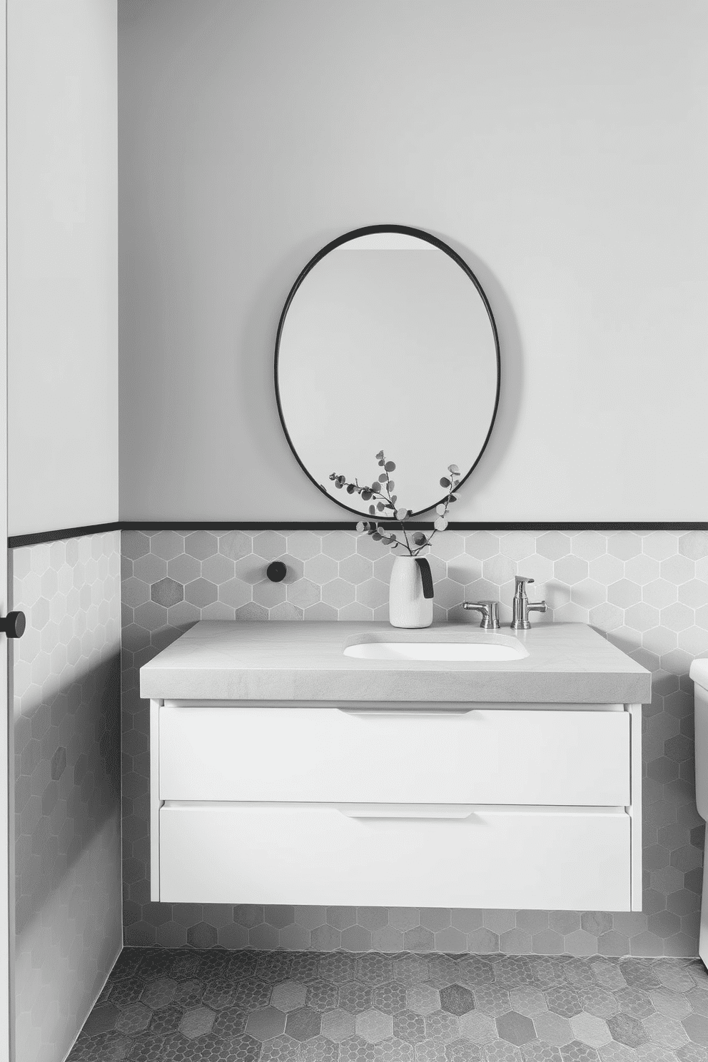 A chic gray bathroom featuring hexagonal tiles with subtle patterns that add texture and dimension to the space. The walls are painted in a soft gray tone, complementing the tiles while creating a cohesive and calming atmosphere. A floating vanity in matte white is topped with a concrete-style countertop, paired with a sleek oval mirror framed in black. Minimalist black fixtures and a delicate arrangement of eucalyptus in a ceramic vase complete the modern aesthetic.