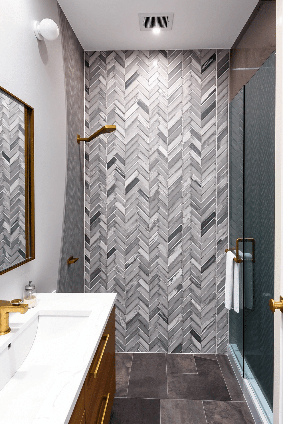 A contemporary bathroom showcasing chevron-patterned gray tiles that elegantly blend modern minimalism with timeless sophistication. The tiles run vertically across the shower wall, while the floor transitions to a smooth slate finish for added texture contrast. A floating wood vanity with a white quartz countertop complements the tiles, adding warmth to the cool-toned palette. Soft recessed lighting highlights the intricate chevron design, while brass accents on the fixtures bring a touch of understated glamour.