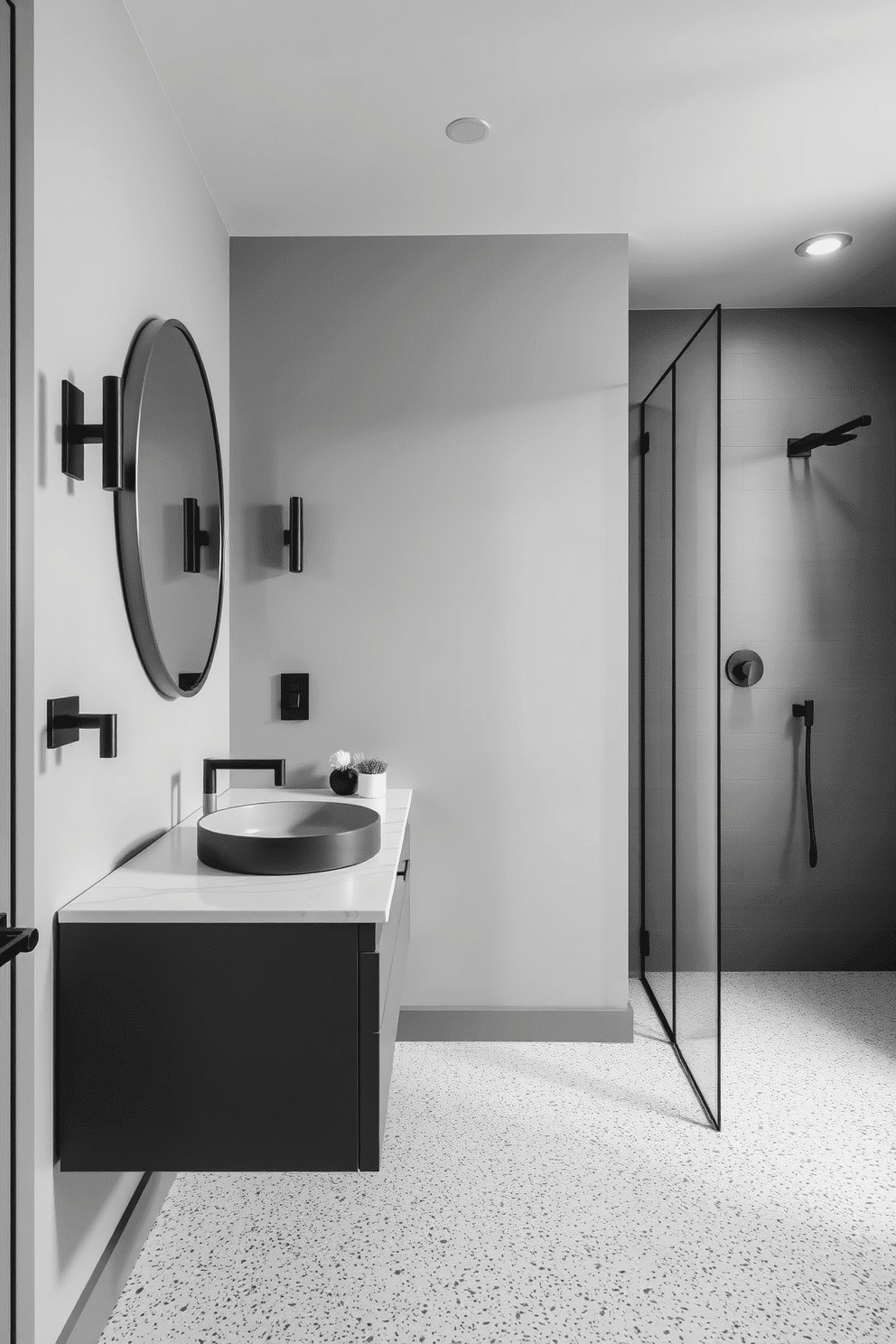 A minimalist gray bathroom with terrazzo flooring that features subtle white speckles, giving the space a modern and polished look. The walls are painted in a soft gray tone, complemented by black matte fixtures and clean, sleek lines throughout the design. A floating vanity with a white quartz countertop adds a touch of refinement, paired with an oversized round mirror framed in brushed silver. Soft lighting emanates from elegant wall sconces, while a large walk-in glass shower with linear black details completes the sophisticated aesthetic.