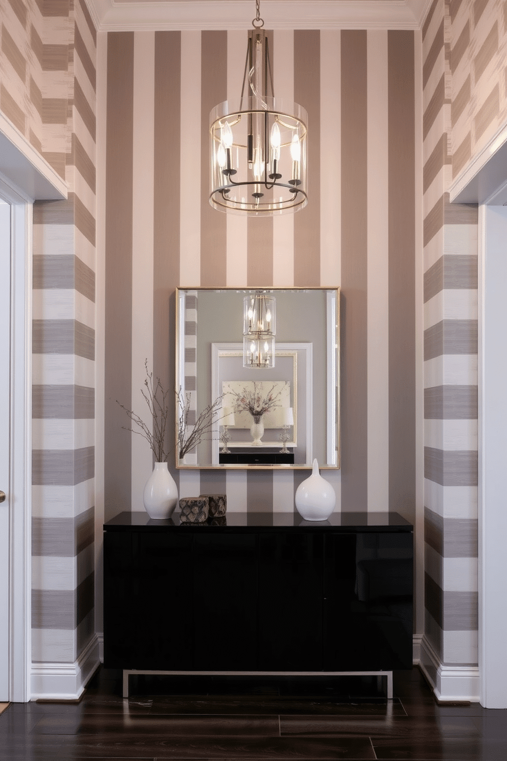 A stunning foyer features gray and white striped wallpaper that adds a touch of elegance and sophistication. The space is illuminated by a modern chandelier, casting a warm glow over a sleek console table adorned with decorative objects and a stylish mirror above it.