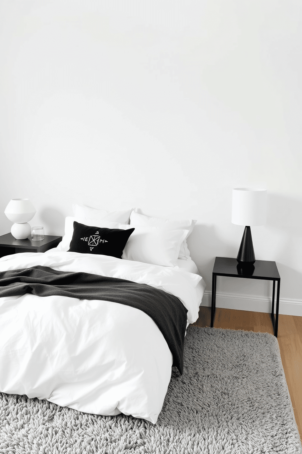 A serene minimalist bedroom featuring a monochrome color palette. The bed is dressed in crisp white linens, topped with a collection of decorative cushions in black, white, and soft gray tones, each showcasing subtle geometric patterns. Beside the bed, a sleek black bedside table holds a modern ceramic lamp in matte white. The room’s walls are painted a soft off-white, and a plush gray area rug lies beneath the bed, adding warmth and texture while maintaining the clean, understated aesthetic.