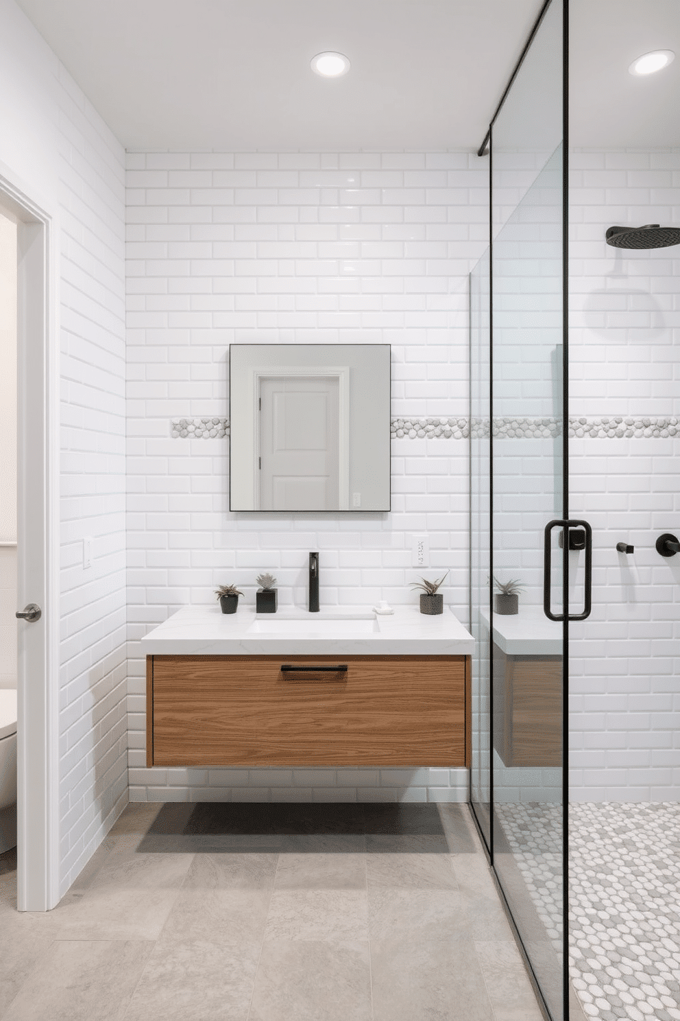 A serene bathroom design featuring a combination of white subway tiles and rounded pebble-shaped mosaic tile inserts on the walls, creating a peaceful and natural spa-like atmosphere. The floor is adorned with large, soft-gray porcelain tiles, while the pebble mosaics subtly trace the outline of the shower area, adding texture and depth. A floating wooden vanity with a light-colored quartz countertop complements the organic aesthetic, paired with a frameless mirror for a modern touch. Minimalist black fixtures, a glass rainfall shower, and small potted plants enhance the natural and balanced design of the space.