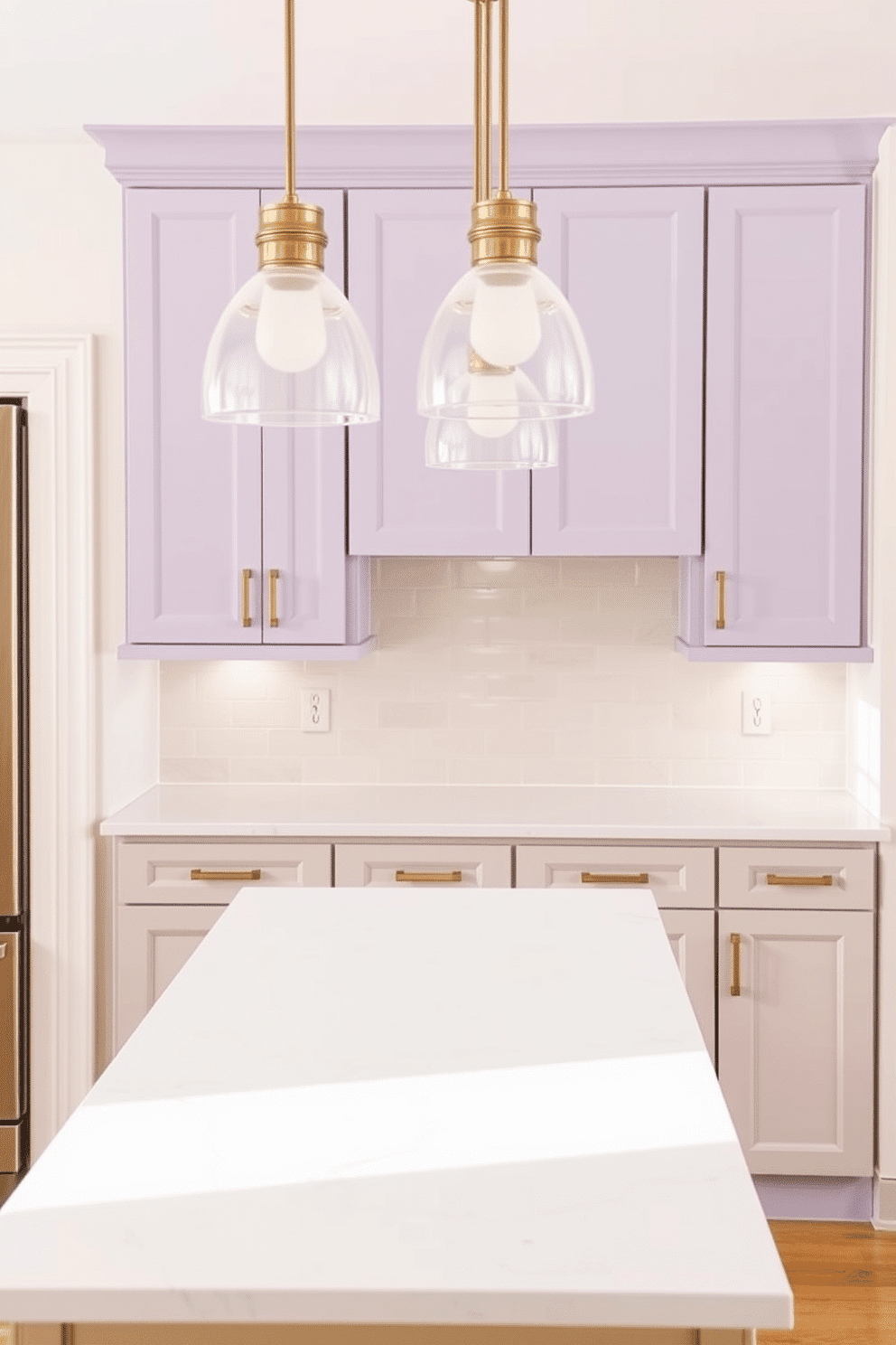 A serene two-tone kitchen with soft lavender upper cabinets and neutral beige lower cabinets. The cabinets are paired with brushed gold hardware, and a pristine white quartz countertop unifies the design. The walls are painted in a subtle off-white shade, allowing the lavender to pop without overpowering the space. A subway tile backsplash in a glossy cream tone reflects natural light, and elegant pendant lights with frosted glass shades hang above a central island.
