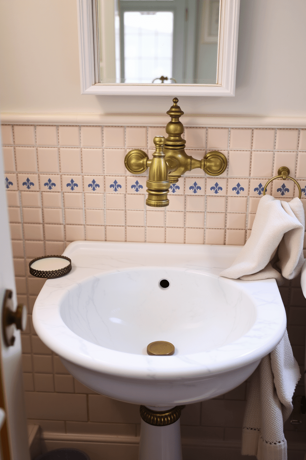 A charming vintage bathroom with a beautifully restored brass faucet, its intricate detailing glistening under soft, natural light. The centerpiece is a polished white marble sink, its surface veined with understated gray patterns that exude timeless elegance. Surrounding the sink is a backsplash of small, hand-painted ceramic tiles in warm cream and soft blue hues. Accessories are kept minimal, with a delicate antique soap dish and a neatly folded linen hand towel adding to the understated luxury.