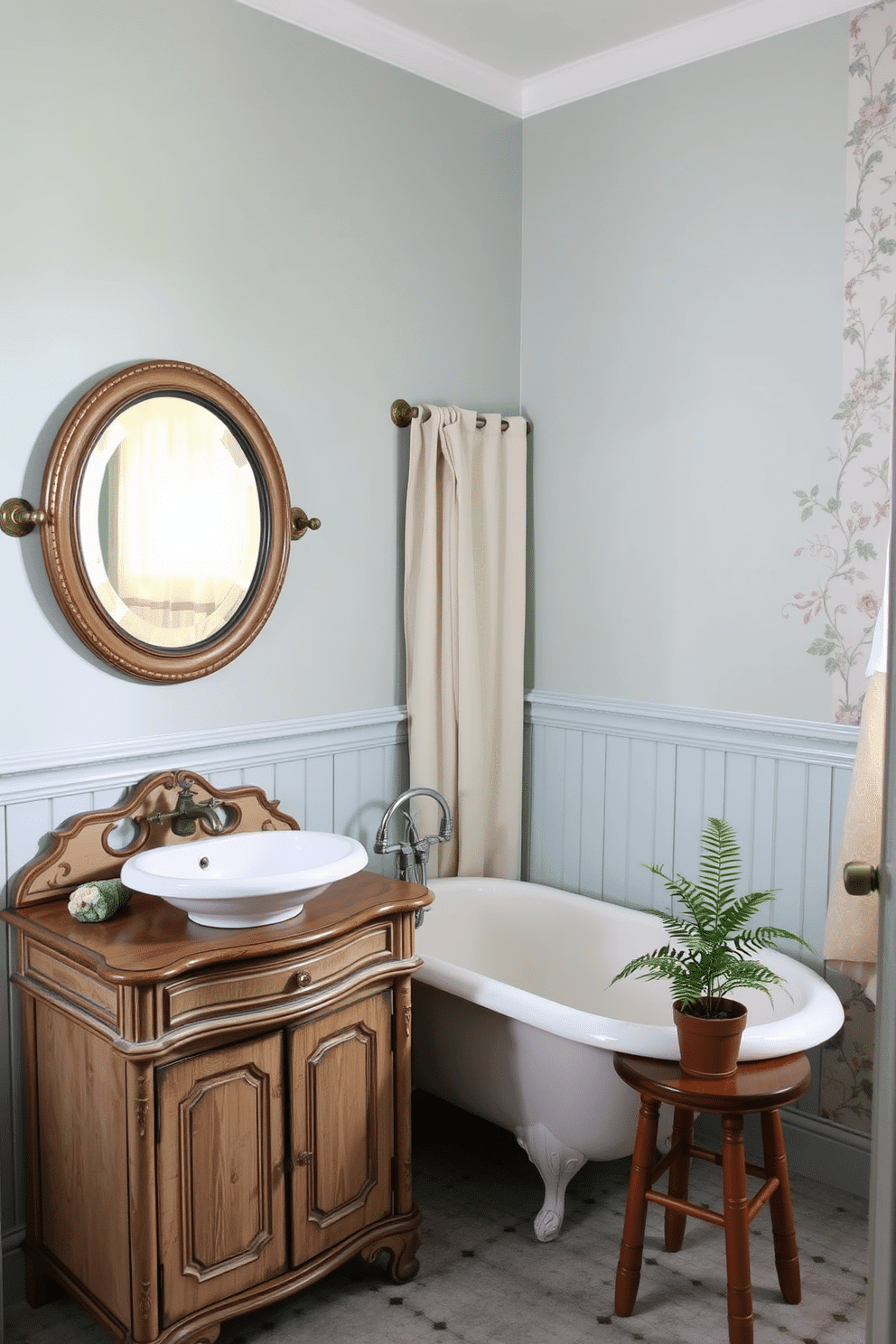 A charming vintage bathroom with a round mirror featuring beveled edges as its focal point. The mirror is framed in distressed wood, hanging above an antique vanity with a white porcelain sink and brass fixtures. The walls are painted in a soft powder blue, adorned with subtle vintage floral wallpaper on one accent wall. A clawfoot tub sits in the corner, surrounded by cream curtains, with a small wood stool nearby holding a potted fern plant.