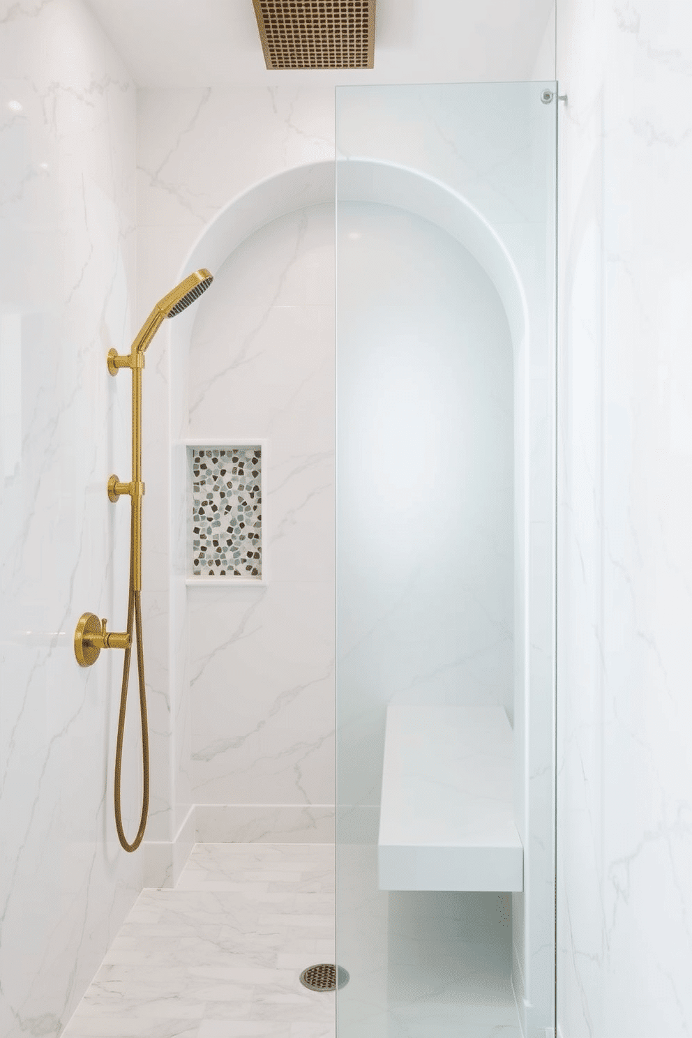A luxurious walk-in shower with a custom arched entryway, surrounded by elegant white marble tiles with subtle grey veining. The shower features brass fixtures, including a rain showerhead and handheld spray, complemented by a built-in niche adorned with geometric mosaic tiles. Adjacent to the arched entry, a sleek bench is integrated into the design, crafted from the same marble for a seamless look. Soft lighting highlights the curves of the arch, while a frosted glass panel provides both privacy and a modern touch to the tranquil space.