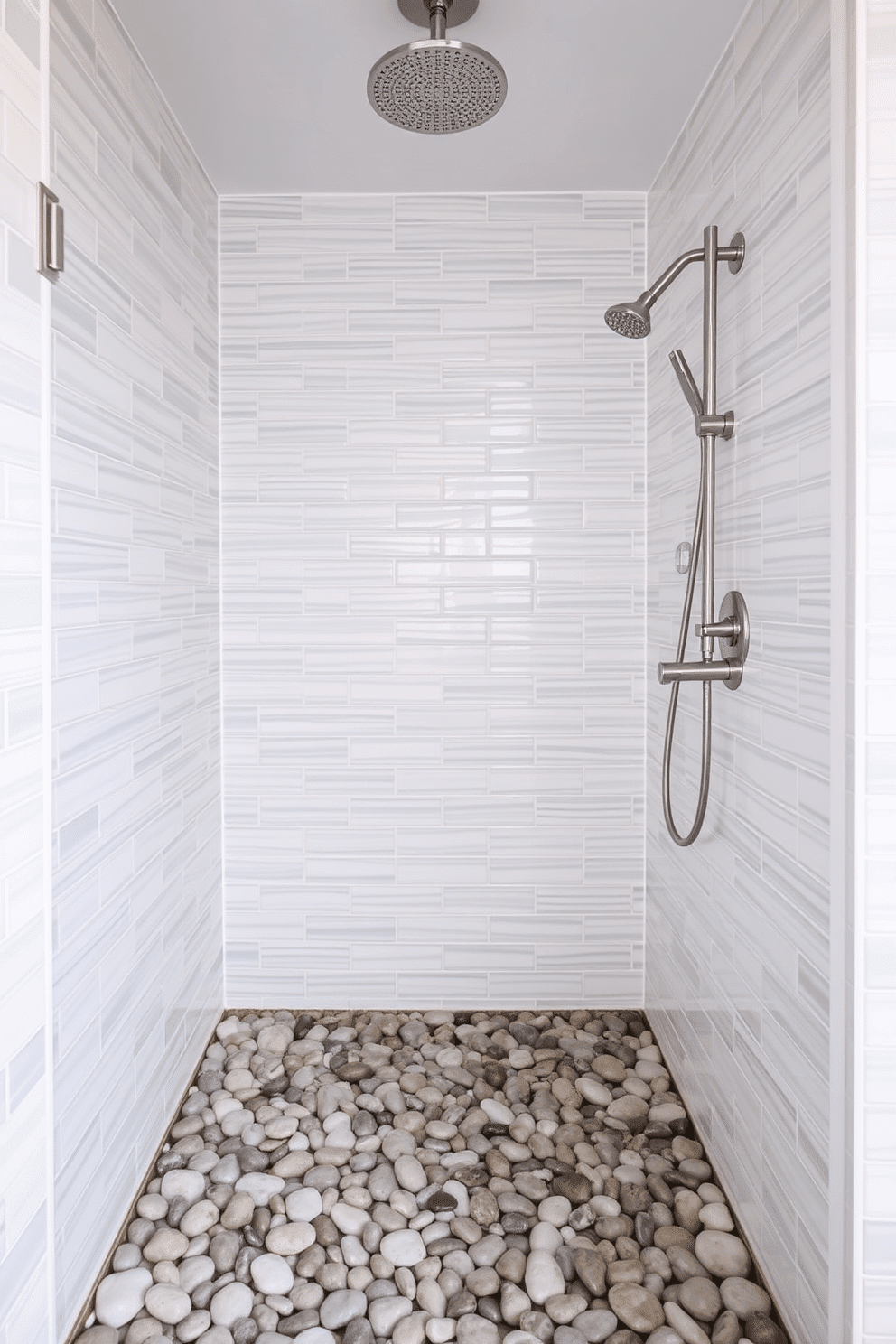 A serene walk-in shower exuding coastal vibes. The shower floor is laid with smooth, natural pebble stones, creating a spa-inspired aesthetic that mimics the feel of a beach shoreline. The walls are tiled in soft, muted tones of seafoam green and white, reflecting the ocean’s tranquility. A rainfall showerhead hangs from above, with minimalist brushed nickel fixtures completing the clean, breezy design.